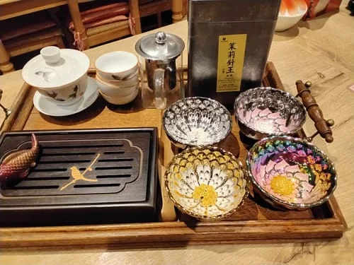 Reviewer's four Vivid Silver bowls with colorful peacock designs arranged on a wooden tea tray with a tea set.