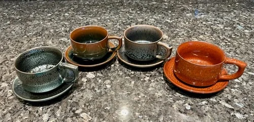 Reviewer shows four Raindrops Coffee Cups in beautiful assorted glazes with matching saucers on a countertop.