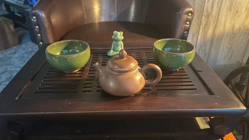 Customer's two green Emerald tea cups on a dark wooden tea tray with a teapot.