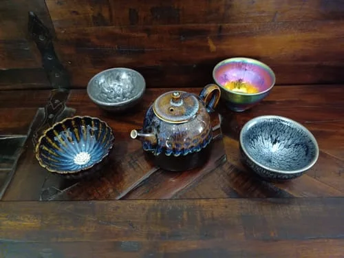 Reviewer's Golden Peacock Teapot with a brown and blue glaze, arranged with four teacups on a wooden surface.