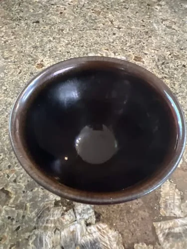 Customer's dark reflective bowl with a brown rim, viewed from above on a stone counter.