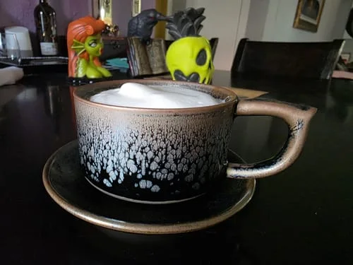 Customer's Raindrops Coffee Cup and saucer on a table, filled with a frothy drink.