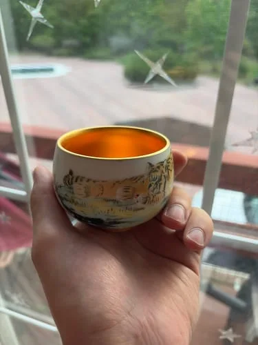 A customer's hand holds The Tiger cup, showing its detailed tiger illustration and shiny golden interior.