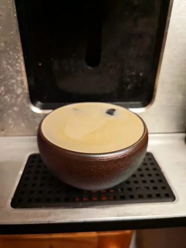 Customer's dark Aurora cup filled to the brim with creamy coffee in a coffee machine.